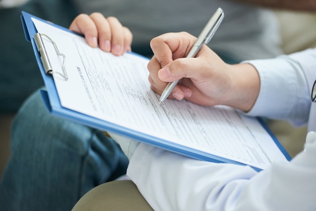 Free Photo hands of unrecognizable female doctor filling in form on clipboard