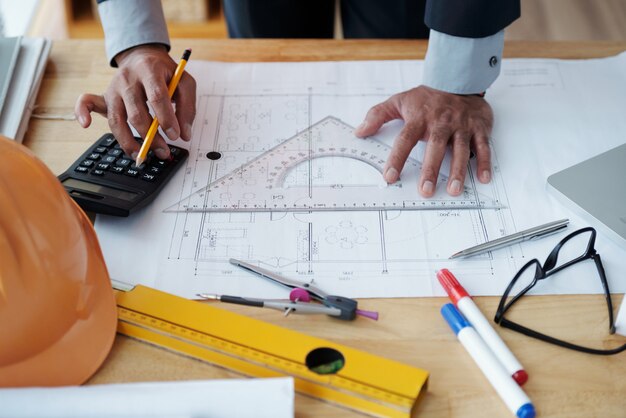 Hands of unrecognizable male architect working on technical drawing and using calculator