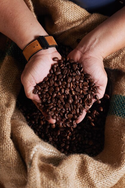 Hands of unrecognizable man holding handful of coffee beans from burlap sack