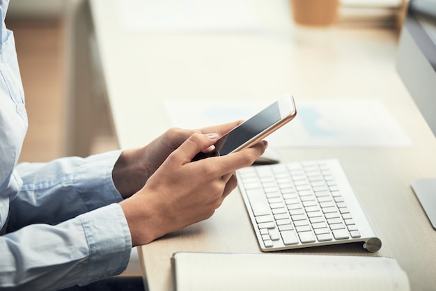 Hands of unrecognizable woman using smartphone at desk in office