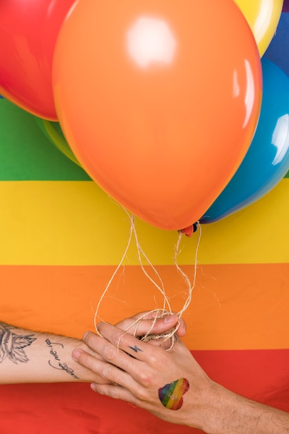 Free photo hands with balloons against rainbow flag