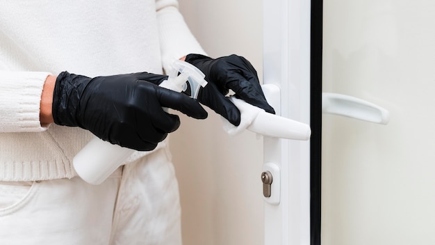 Hands with gloves disinfecting door handle