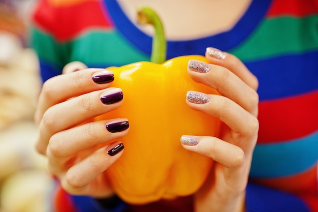 Free photo hands with manicure of young girl wear in colored sweater holing red sweet pepper