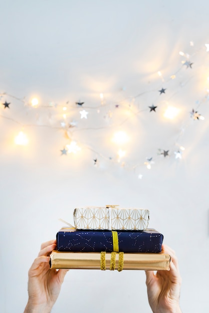 Free photo hands with present boxes near fairy lights and ornament stars