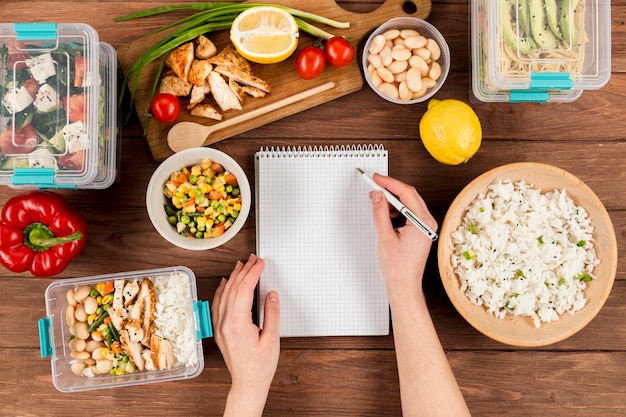 Hands writing on notebook with casseroles ad food