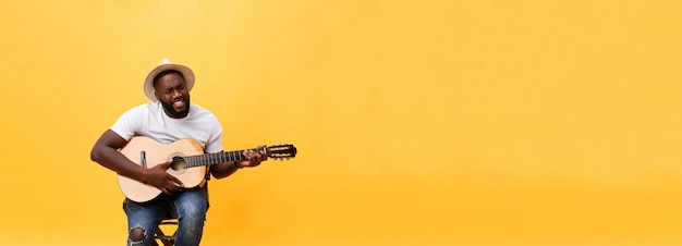 Free photo handsome african american retro styled guitarist playing acoustic guitar isolated on yellow backgrou