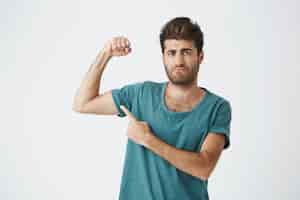 Free photo handsome athletic italian unshaven guy in blue shirt, with concentrated expression showing his muscles after month of training in gym.