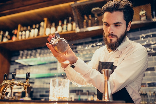 Handsome bartender making drinking and cocktails at a counter