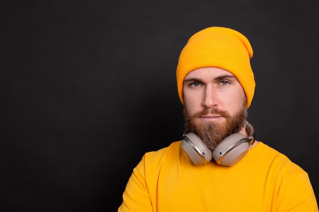 Free photo handsome bearded  hipster man yellow hat t shirt with headphones isolated on black  background