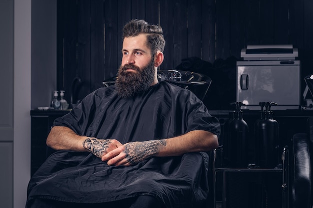 Free Photo handsome bearded male with a tattoo on his arms before hair wash in a hairdressers salon.