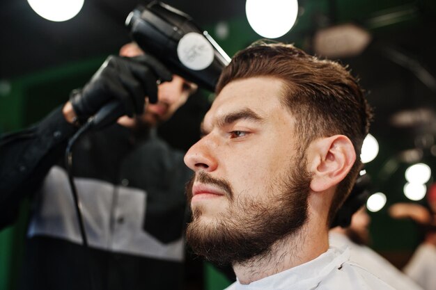 Handsome bearded man at the barbershop barber at work using hair dryer