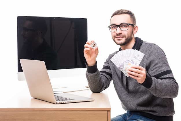 Free photo handsome bearded man at his working place with laptop and pc monitor screen on back with bitcoin and dollars cash in hands