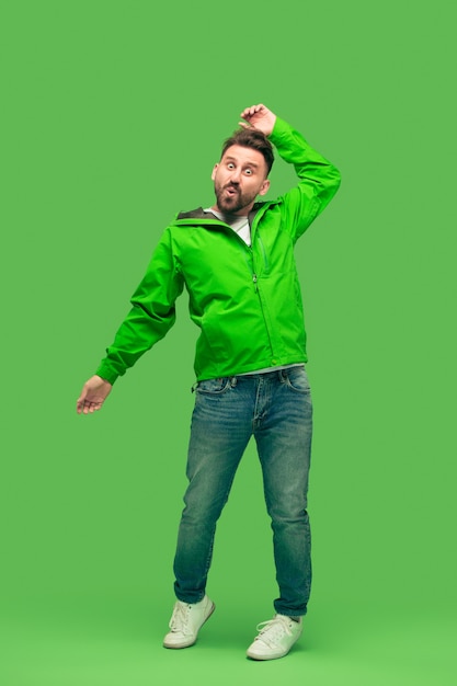 Free photo handsome bearded smiling happy young man looking at camera isolated on vivid trendy green studio. concept of the autumn and cold time