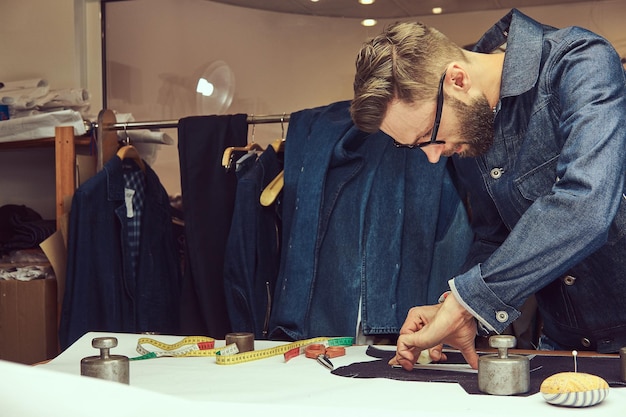 Free photo handsome bearded tailor working with cloth samples at a sewing workshop.