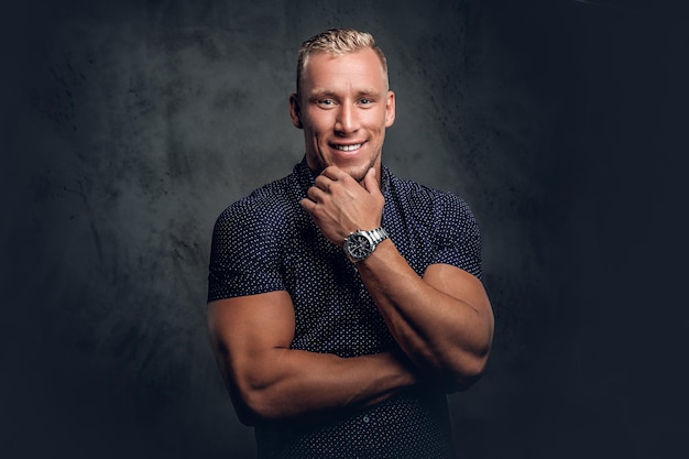 Handsome blond man in a dark blue shirt posing over grey background in a studio.