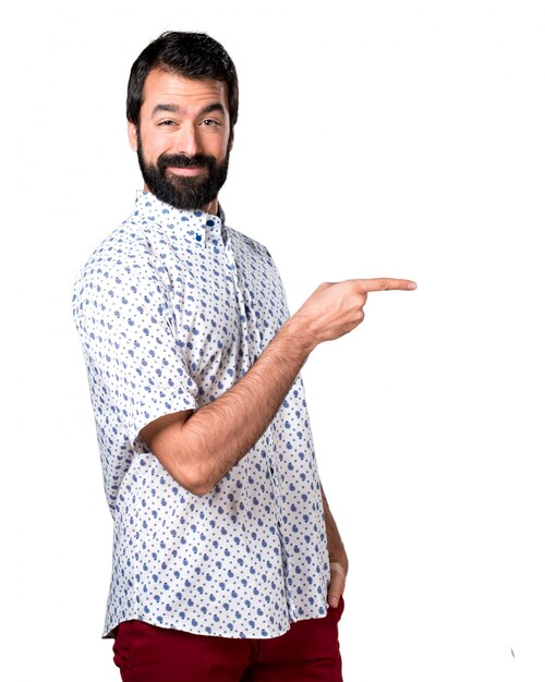 Handsome brunette man with beard pointing to the lateral