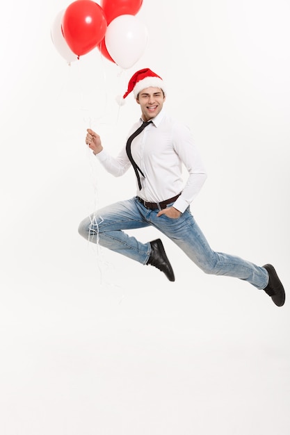 Free Photo handsome business man jumping for celebrating merry christmas wearing santa hat with red balloon.