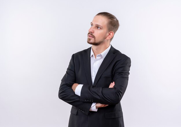 Handsome business man wearing suit looking aside with pensive expression standing over white background