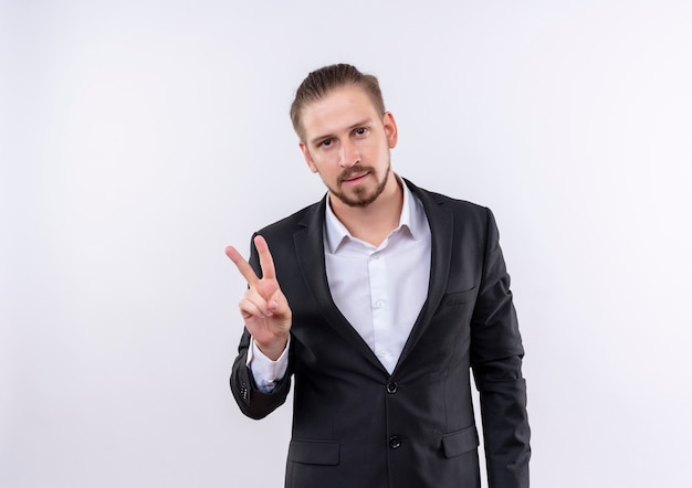 Handsome business man wearing suit looking at camera smiling confident showing victory sign standing over white background