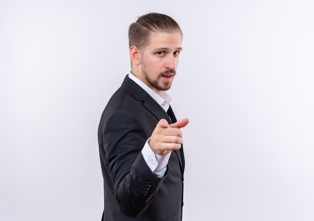 Handsome business man wearing suit looking confident pointing with finger to camera standing over white background