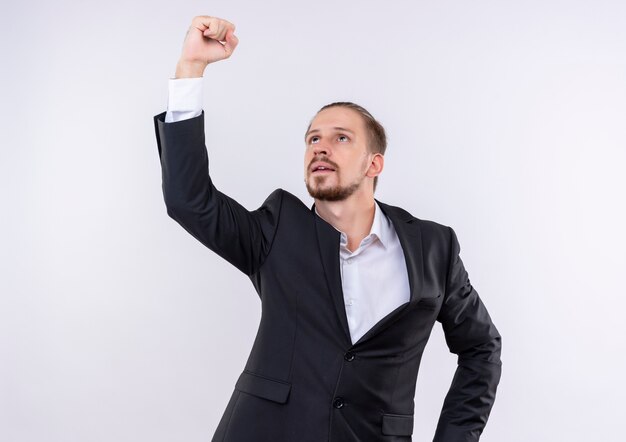 Handsome business man wearing suit looking up showing fist with serious face standing over white background