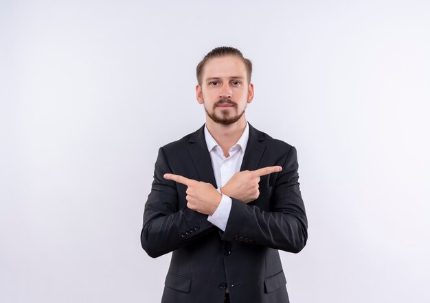 Handsome business man wearing suit pointing with index fingers to the sides standing over white background