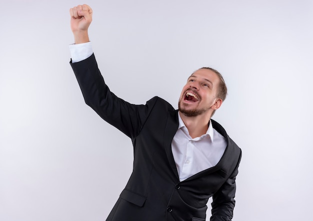 Handsome business man wearing suit raising fist crazy happy standing over white background