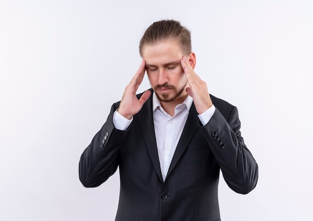 Handsome business man wearing suit touching his temples looking tired and overworked having headache standing over white background