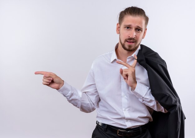 Handsome businessman carrying his jacket on shoulder looking at camera smiling confident pointing with figers to the side standing over white background