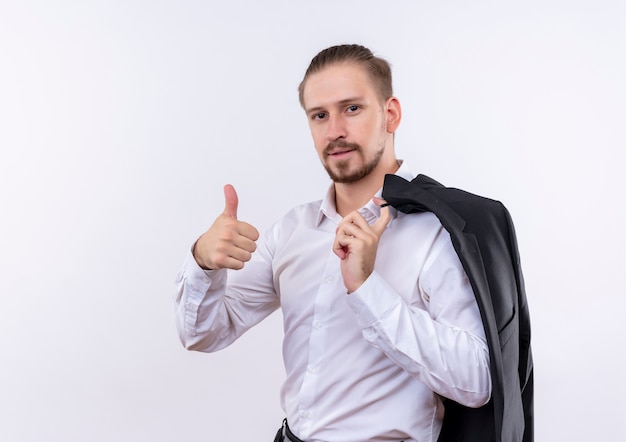 Handsome businessman carrying his jacket on shoulder looking at camera with confident smile showing thumbs up standing over white background