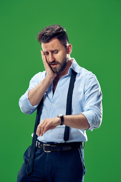 Handsome businessman checking his wrist-watch isolated on green background.