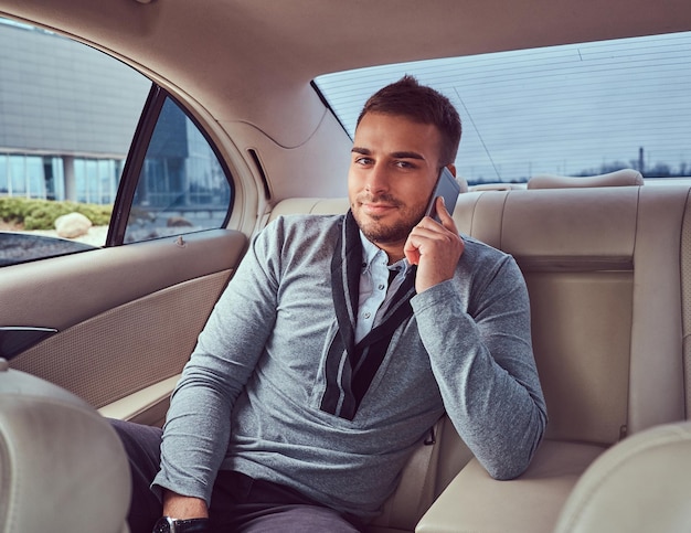 Free photo a handsome businessman in elegant clothing working, talking on the phone while sitting in the car.