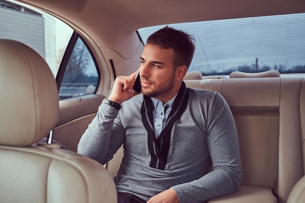 Free photo a handsome businessman in elegant clothing working, talking on the phone while sitting in the car.