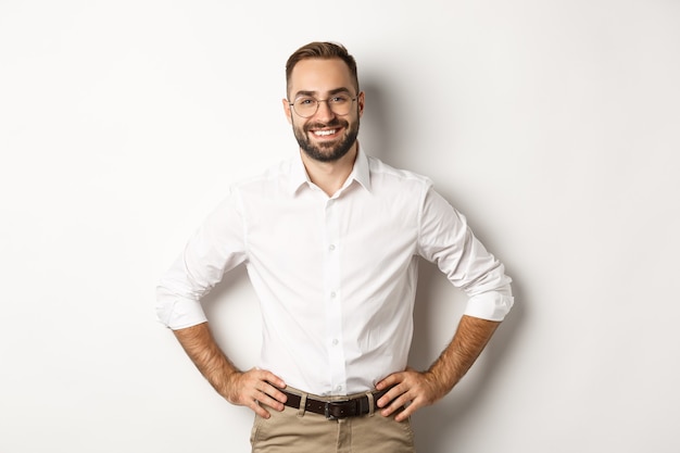 Handsome businessman in glasses looking satisfied, smiling and holding hands on waist, standing  