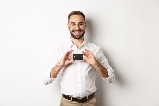 Handsome businessman holding a card, smiling satisfied, standing  