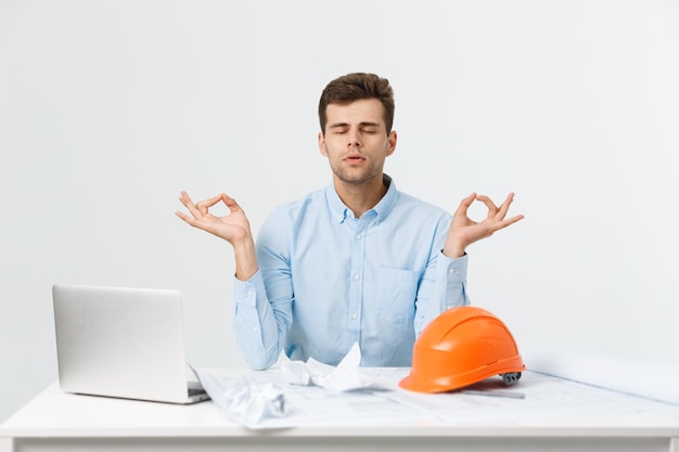 Free photo handsome businessman is relaxing in the office, sitting in a traditional yoga lotus position.