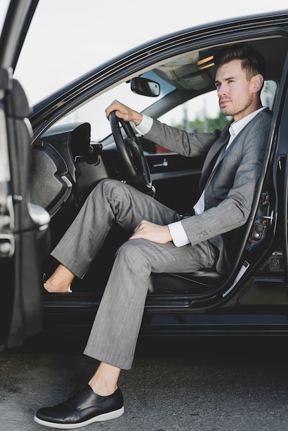 Free photo handsome businessman sitting in the car with open door