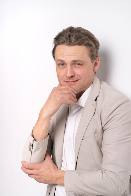 Handsome businessman standing with hand touching his chin looking at camera and smile wearing white shirt and cream jacket on white background Business concept