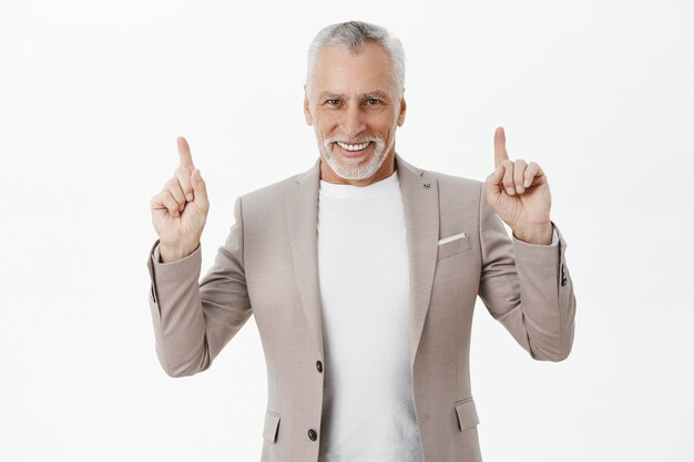 Handsome businessman in suit pointing fingers up and smiling pleased