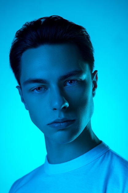 Handsome caucasian man's portrait isolated on blue studio background in neon light, monochrome. Beautiful male model. Concept of human emotions, facial expression, sales, ad, fashion and beauty.