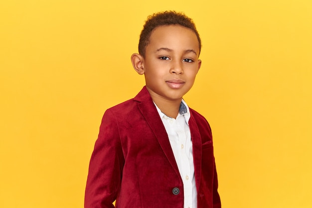 Handsome cute African American little posing isolated having confident facial expression, smiling, wearing trendy crimson velvet jacket.