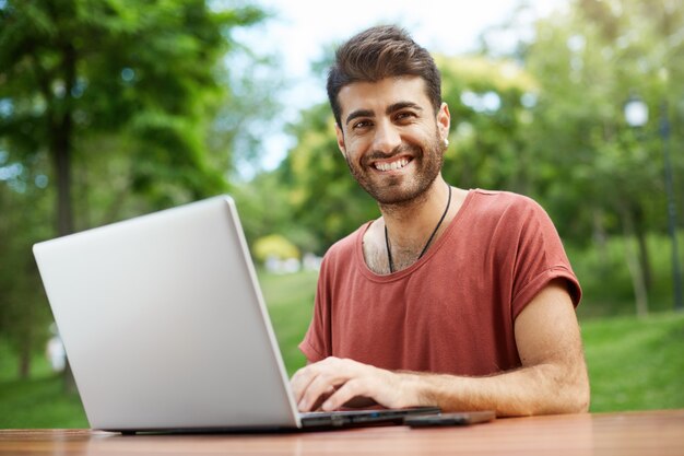 Handsome freelancer working remote, sit on park bench with laptop, connect wifi