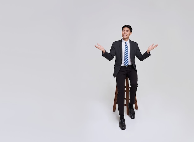 Handsome and friendly face asian businessman smile in formal suit points his hands to presented to copy space on white background studio shot.