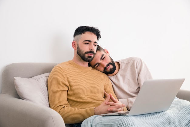 Free photo handsome gay couple sitting together on sofa looking at laptop