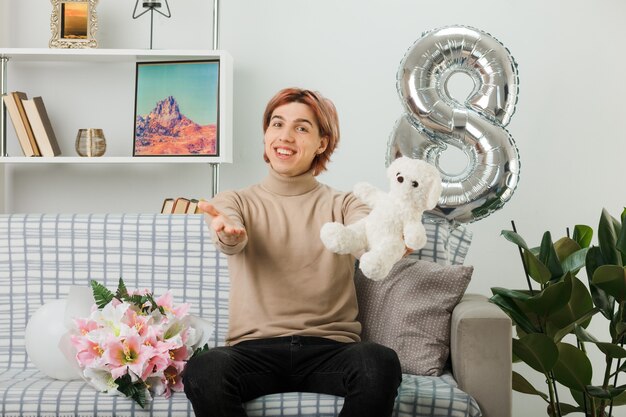 Handsome guy on happy women day holding teddy bear sitting on sofa in living room