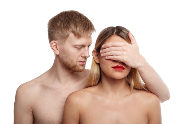 Free Photo handsome guy with light hair and stubble standing shirtless behind attractive naked female and covering her eyes with palm. people, relationships, intimacy, feelings, sexual life and closeness