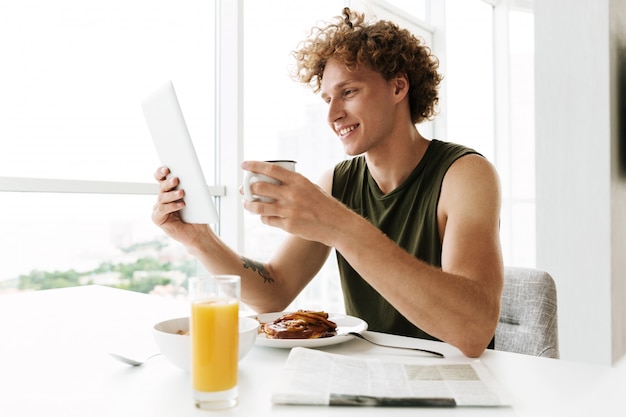 Handsome happy man using tablet computer and drinking coffee