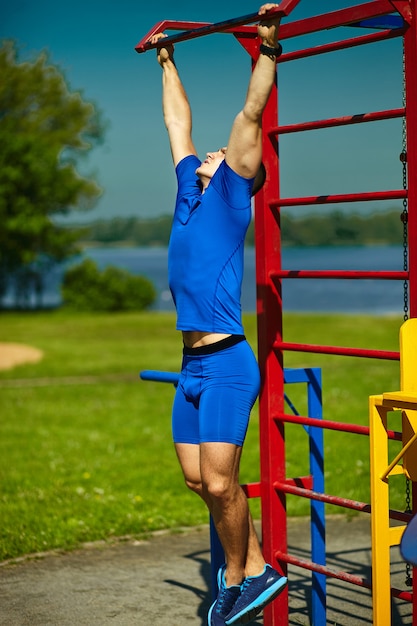 Handsome healthy happy srtong athlete male man exercising at the city park - fitness concepts on a beautiful summer day on horizontal bar