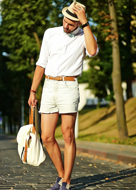 Free photo handsome hipster model man in stylish summer clothes posing  in hat with bag