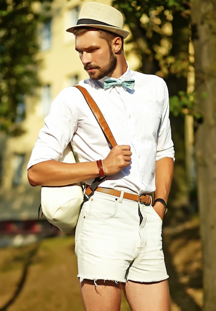 Free photo handsome hipster model man in stylish summer clothes posing  in hat with bag